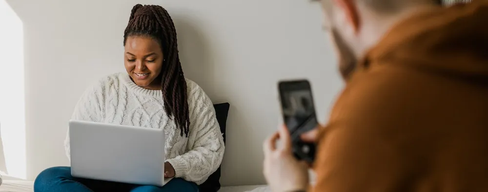 Cheerful african american woman blogger with laptop while guy making photo for blog or social media. Man taking picture girl when she writing post on social media vlog